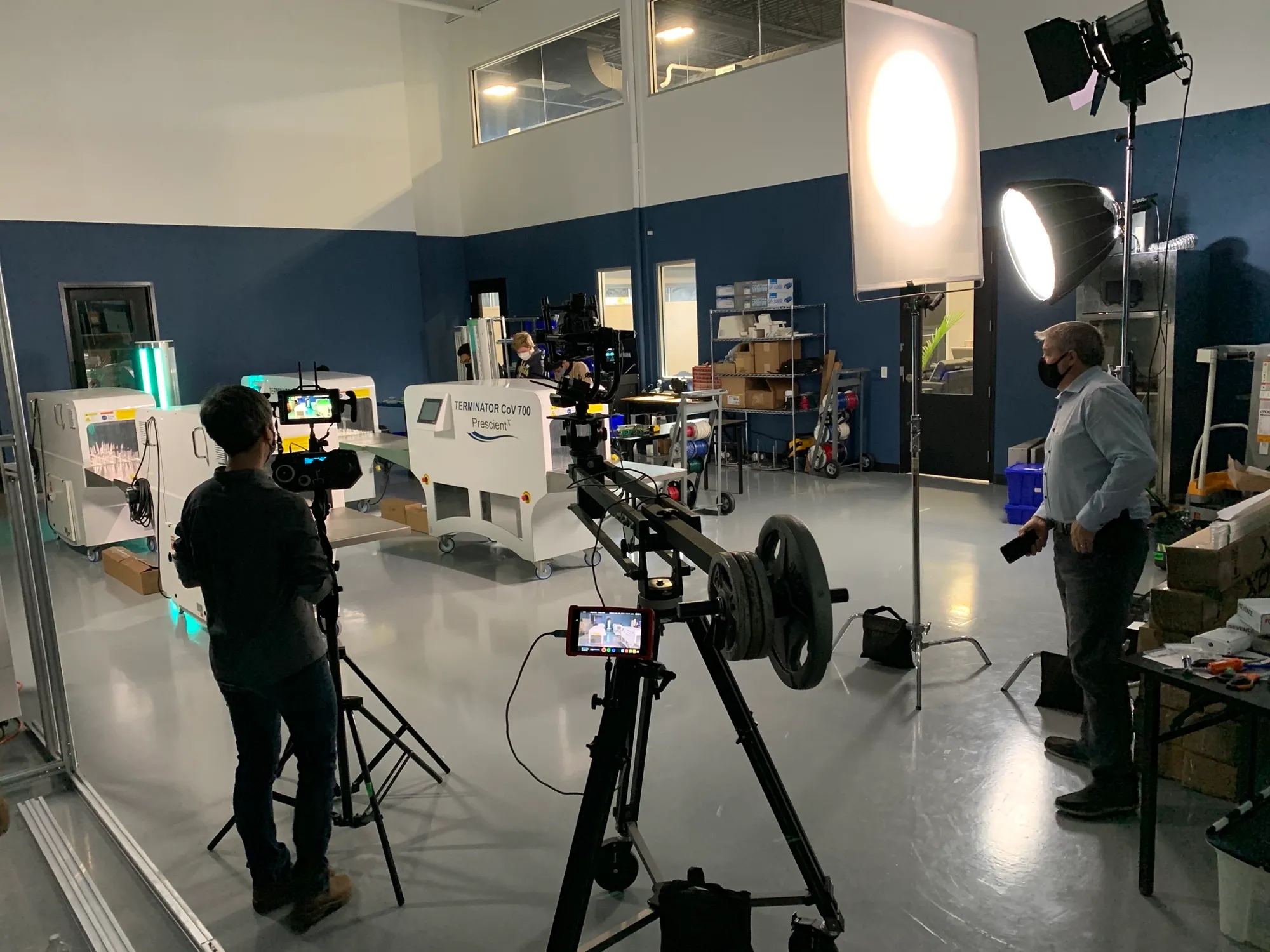 A crew shooting a product on a camera slider in a studio, lit by a large softbox, with a crew member in frame.