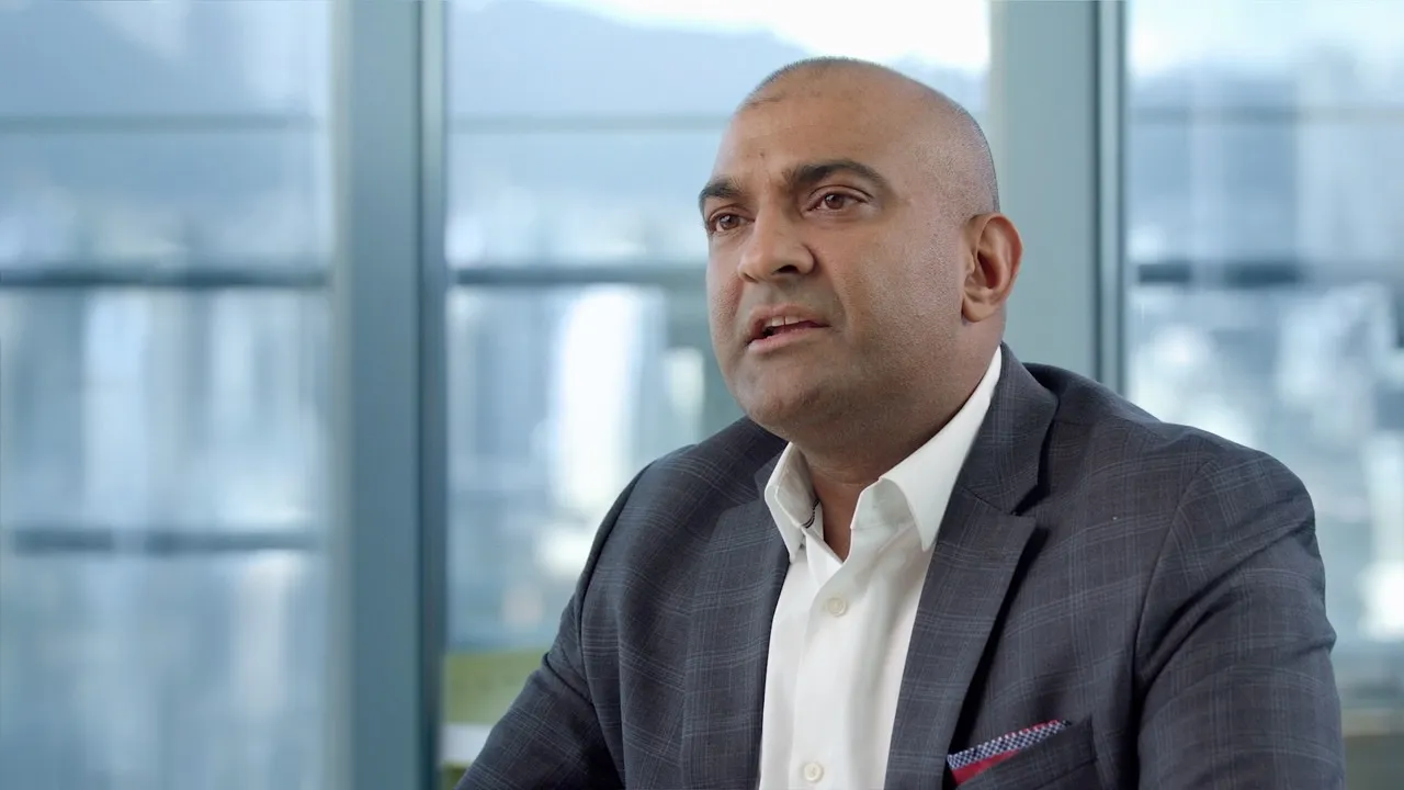 A finished interview frame from the film: Microsoft’s Raj Cheema mid-answer, framed against the Vancouver skyline and mountains through floor-to-ceiling glass.