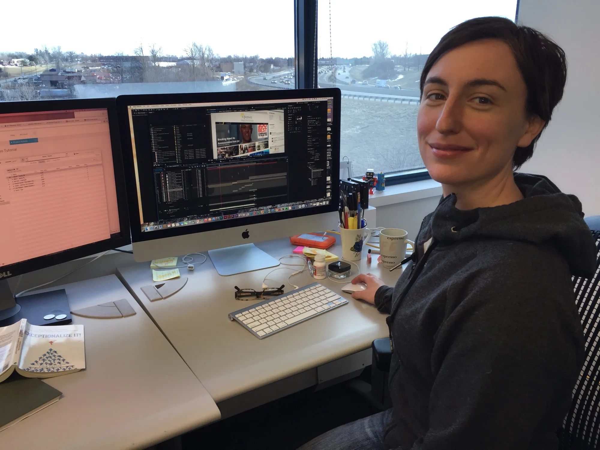 Kate seated at a dual-monitor editing workstation, turning to the camera with a video-editing timeline open on the screen behind her